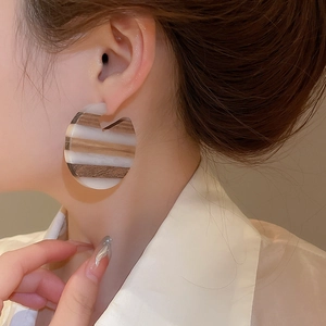 Close-up of geometric C-shaped earrings with wood texture and white resin on a model