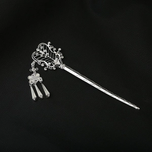 Detail of silver hollowed hair stick with tassels on black textured leather surface