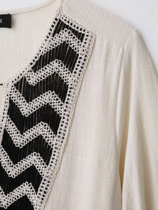 Detailed close-up of bohemian embroidered neckline with black and white wavy crochet trim