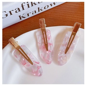 Detail of three pink acrylic hair clips with seashell fragments on a white decorative plate