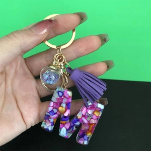 Detail of resin letter M keychain with purple tassel and glitter star ball in hand