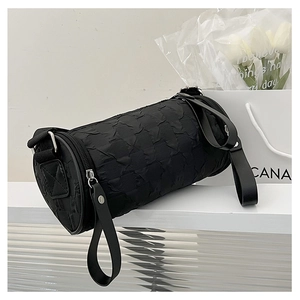 Close-up of black cylindrical shoulder bag with quilted texture on white geometric stand