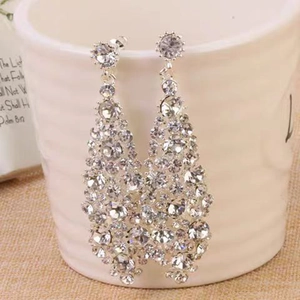 Close-up of long tiered rhinestone drop earrings hanging on a white ceramic cup