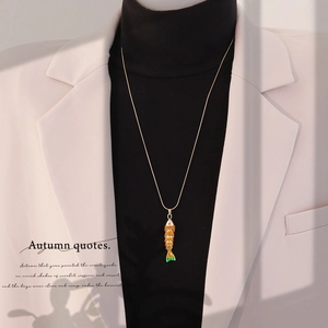 Detail of a vintage 3D koi fish pendant on a long gold chain over a black sweater