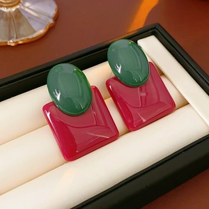 Close-up of geometric resin earrings in red and green colors on a white velvet cushion