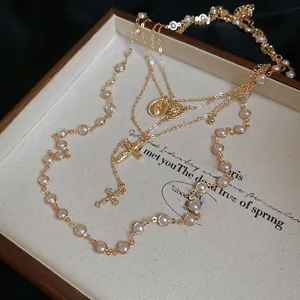 Detailed view of layered gold necklace with pearl strand, cross charms and holy medals