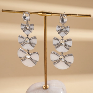 Detail of bow-shaped dangling earrings with resin pearls and shimmering rhinestones