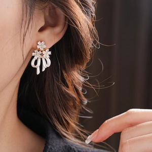 Gros plan de boucles d'oreilles nœud dorées avec pétales blancs et zircons scintillants
