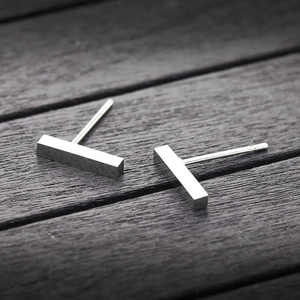 Minimalist polished stainless steel bar stud earrings on a grey wood texture background