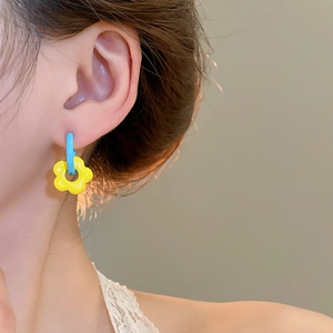 Close-up of asymmetrical blue and yellow flower drop earrings worn on model's ear