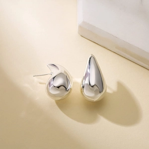 Minimalist silver teardrop earrings in polished titanium steel on a warm background