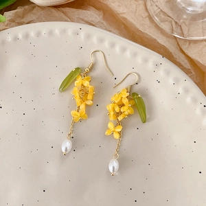 Detail of yellow flower earrings with green leaf accents and white pearl drop charms