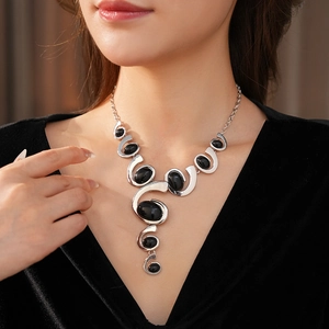 Close-up of model wearing a silver abstract swirl necklace with black oval gemstones