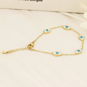 Gold-plated evil eye chain bracelet with five blue enamel charms on white linen fabric