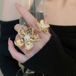 Detailed view of irregular gold flower ring featuring textured petals and a centered pearl