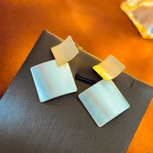 Macro detail of square geometric stud earrings with brushed gold and silver metal textures