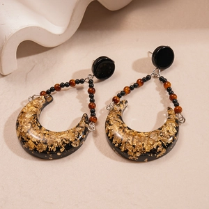 Detail of vintage moon earrings with gold foil resin on a beige stone surface