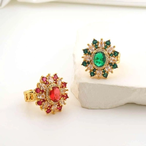 Close-up of gold rings with red and green gemstones on white stone background