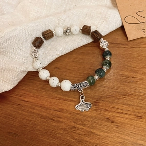 Detail of beaded ceramic bracelet with silver ginkgo leaf charm and wooden elements