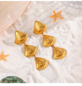 Gouden schelpoorbellen met drie lagen gepresenteerd op zand met een zeester-decor