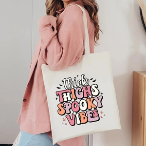 Detail of white canvas tote bag with Thick Thighs Spooky Vibes print and bat motifs