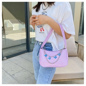 Detail of purple shoulder bag with blue butterfly charms and metal chain on a model