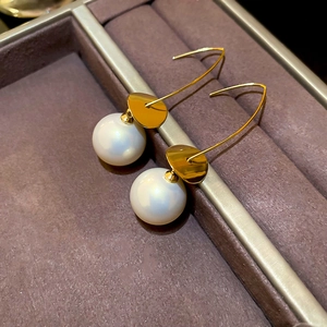 Close-up of gold dangle earrings with pearls and metallic sequins on a velvet tray