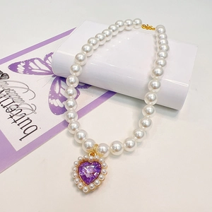Macro detail of elegant pearl pet collar with a purple heart crystal pendant and gold clasp