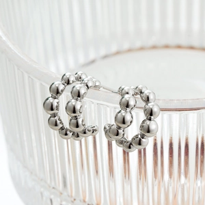 Macro view of C-shaped silver bubble hoop earrings hanging on striped glass texture