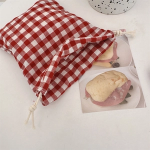 Detail of red and white checkered drawstring bag with woven rope on a white desk