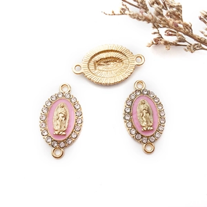 Dettaglio macro di ciondoli religiosi in smalto rosa e strass con base in lega dorata