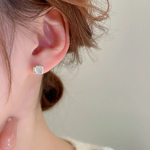 Elegant square silver earrings with round cat-eye stone on a model's ear