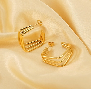 Detail of 18K gold-plated triple hoop earrings on elegant silk background fabric