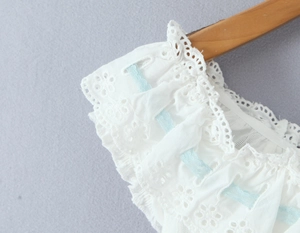 Close-up of white lace blouse detailing with blue ribbon and eyelet embroidery detail