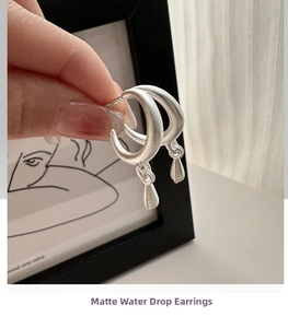 Close-up of matte silver oval earrings with small teardrop pendants on S925 silver