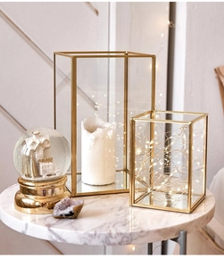 Detail of modern gold metal frame glass candle holders on a marble table with warm lighting