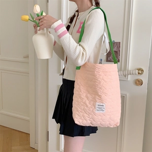 Quilted heart tote bag with green contrast straps worn by a model in a cozy setting