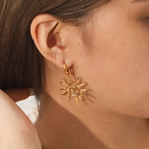 Detailed close-up of a model wearing gold sun-shaped earrings with hammered texture