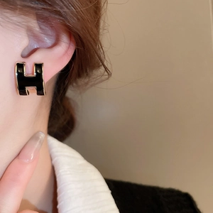 Close-up of black and gold H-shaped enamel earrings worn by a model on the ear