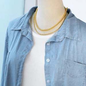 Detail showing a layered golden ball chain necklace on a model wearing denim clothes