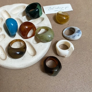Flat lay of colorful oval resin rings on a stone tray with vintage paper aesthetic