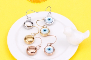 Detailed view of Evil Eye drop earrings in gold, silver, and rose gold on a yellow background