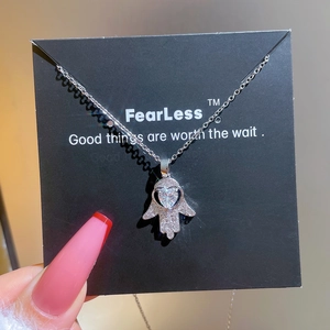 Detail of silver Hamsa Hand necklace with heart zircon on a black display card
