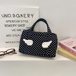 Close-up of polka dot travel bag with white plush wings on a decorative tabletop