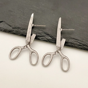 Detailed close-up of retro silver scissor-shaped stud earrings on a textured stone surface