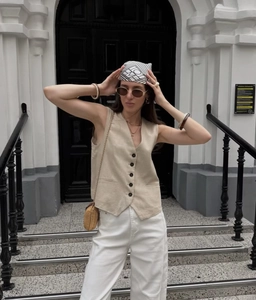 Detailed view of a beige linen blend V-neck vest with black buttons on a female model