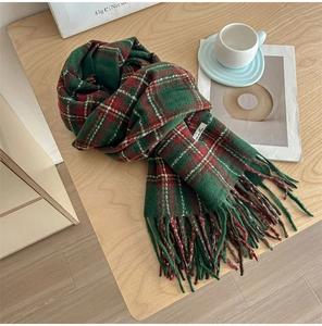 Detail of red and green plaid winter scarf with fringe tassels on wooden background