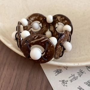 Close-up of vintage coconut shell and white bead bracelet on a ceramic plate