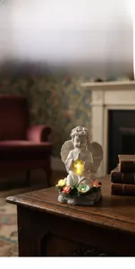 Detail van biddend engelbeeld met lichtgevend kruis en kleurrijke bloemen op de voet