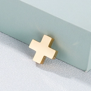 Polished gold stainless steel cross pendant on a minimalist grey textured surface